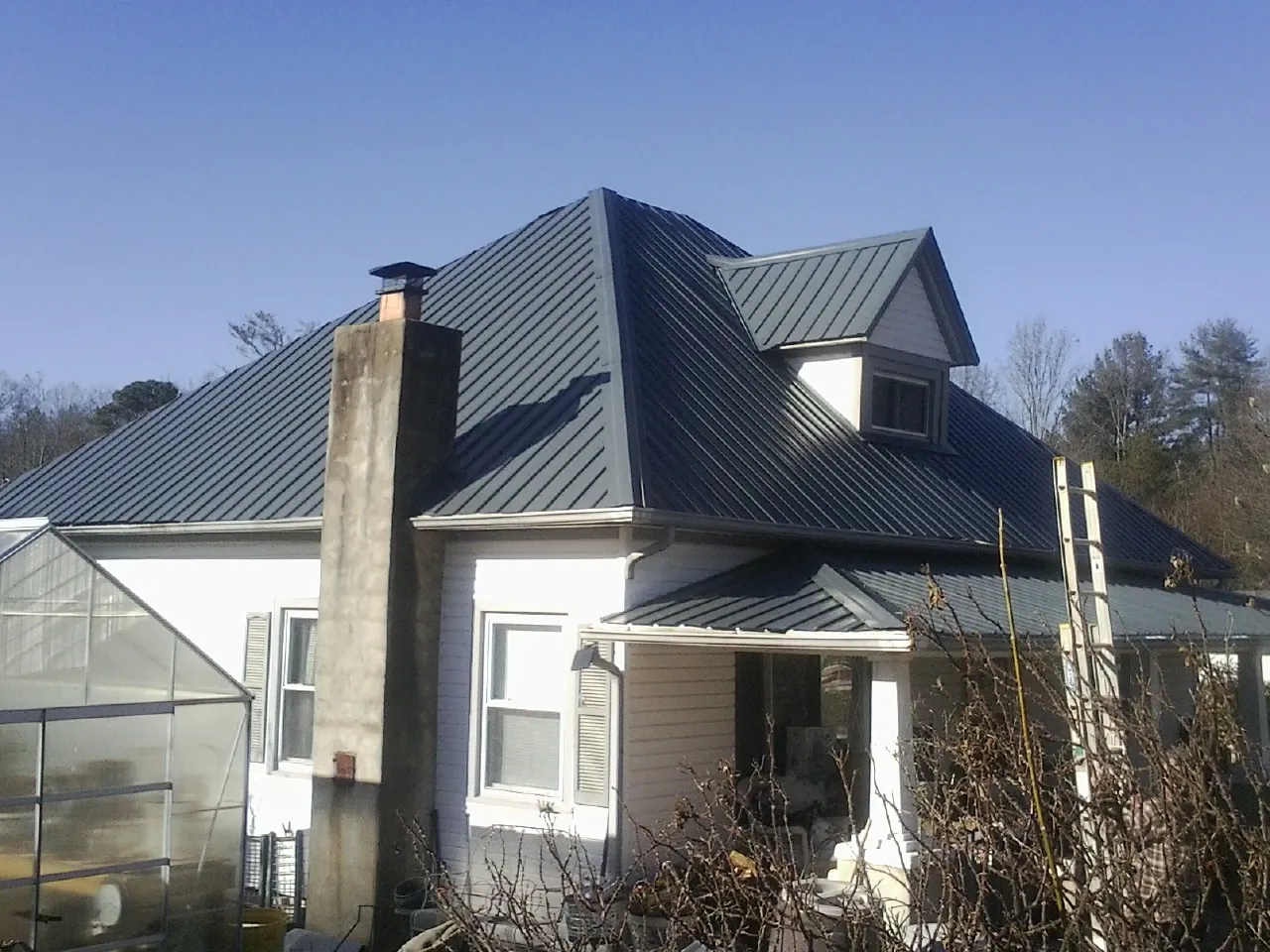 Dark blue standing seam metal roof on a white farmhouse with dormer — Slate & Tile Roof Repair by Roofing Brothers in Wellsburg