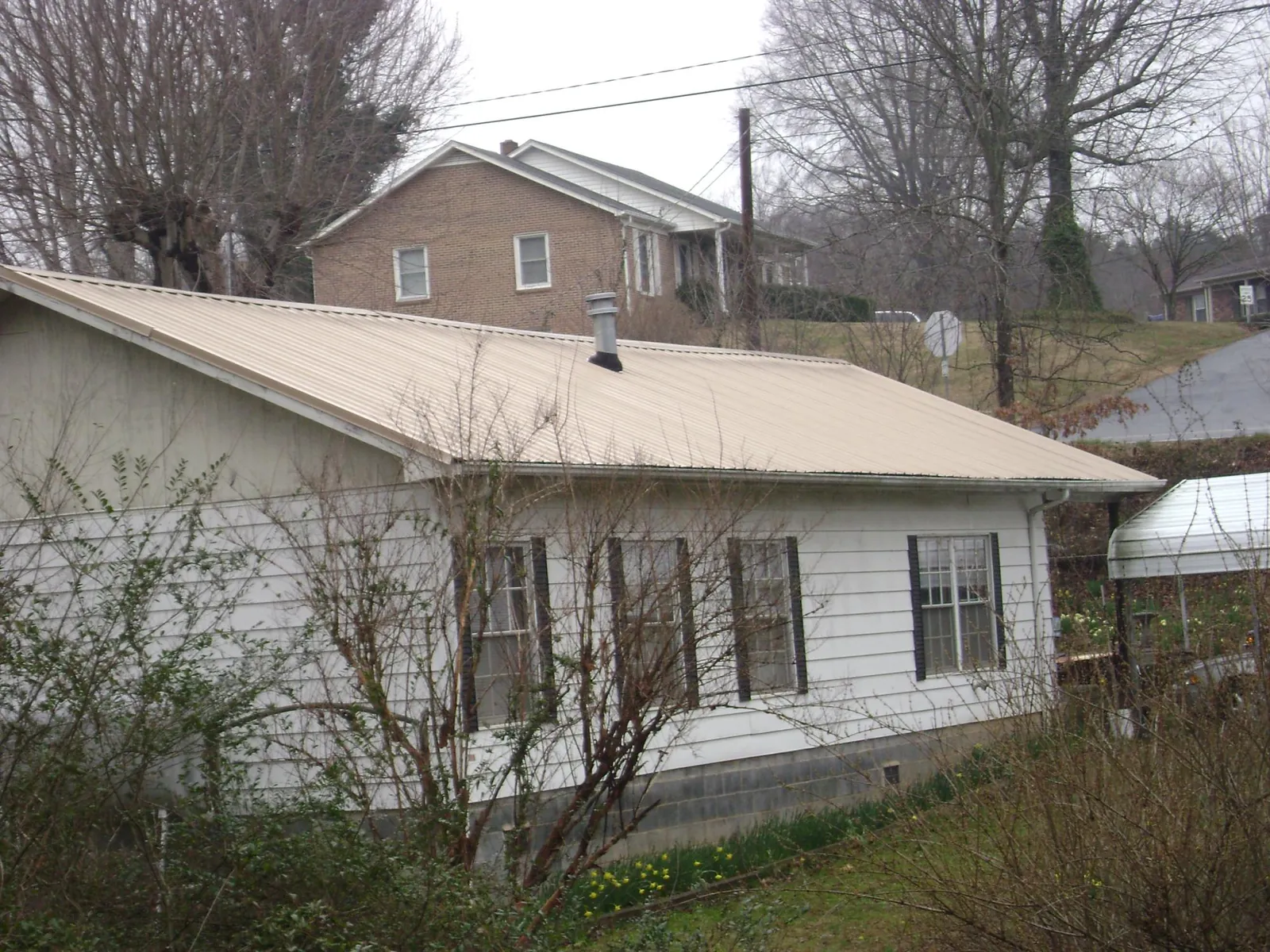 Tan metal roof on a white sided house set into a hillside — Commercial Roofing by Roofing Brothers in Wellsburg